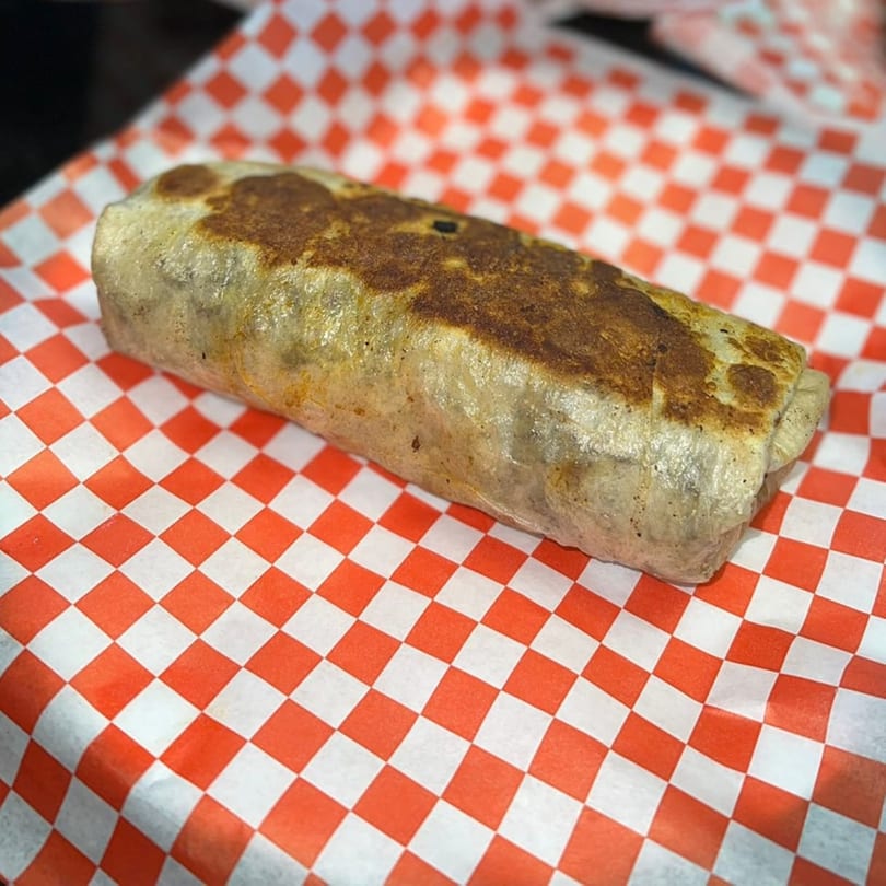 A large, golden-brown burrito from El Taco Loko rests on red and white checkered paper.