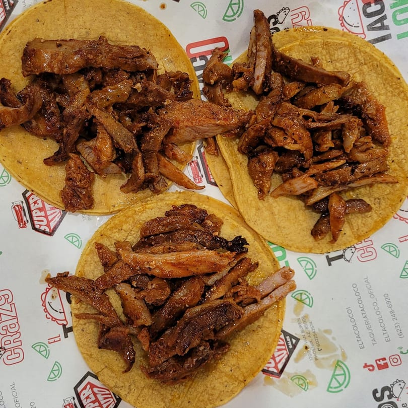 Three El Taco Loko tacos with seasoned meat on corn tortillas, on branded paper.