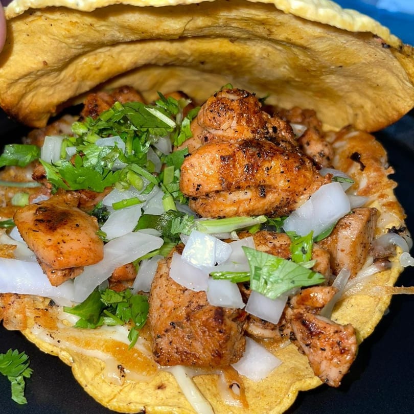 A close-up of a Mexican taco with seasoned chicken, diced onions, and fresh cilantro on a tortilla.